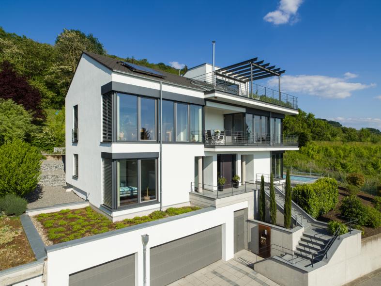 Großzügige Fensterfassade in Holz-Alu mit teilweise sichtbaren Raffstorekästen